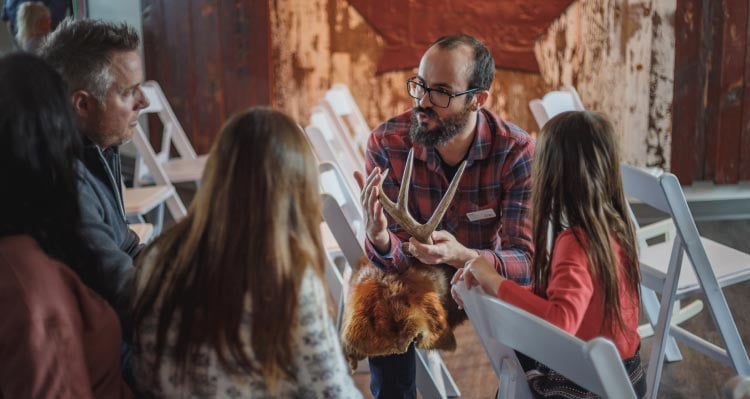 A man holds a deer's antler talking with guests.