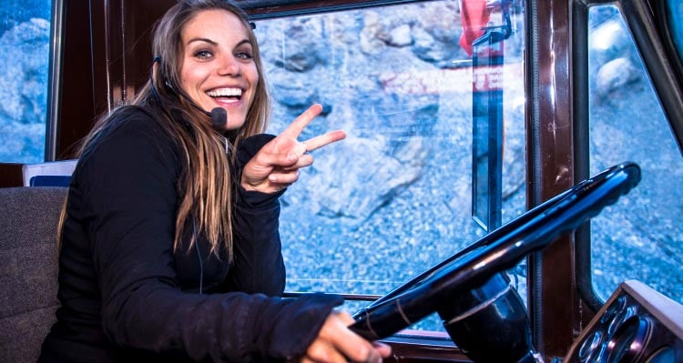 A bus driver smiles and holds up a peace sign.