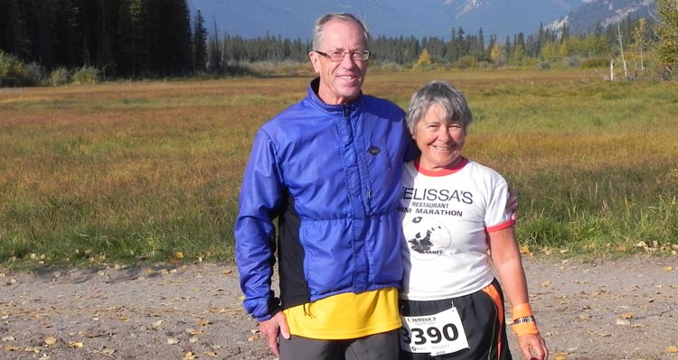 Two people dressed for a run stand in front of a grassy meadow.