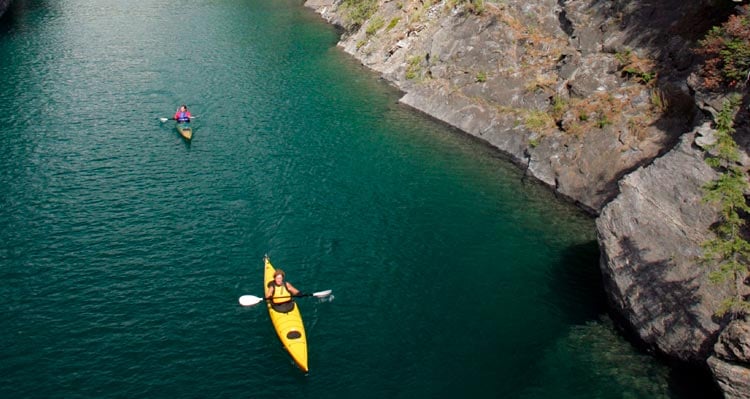 Two kayakers paddle down a river between steep rock walls.