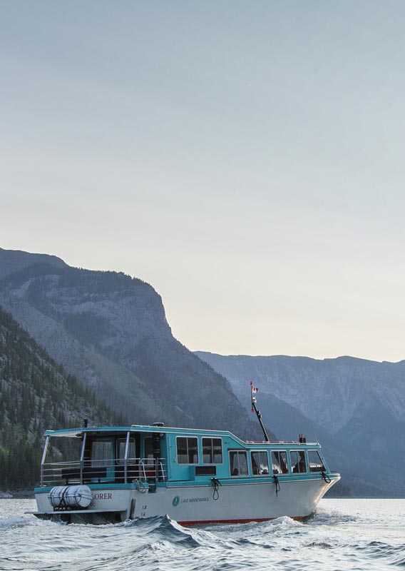 A blue and white boat cruises on a mountain lake towards the rising sun.