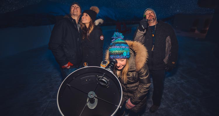 Four people group around a telescope to look up at the night sky.