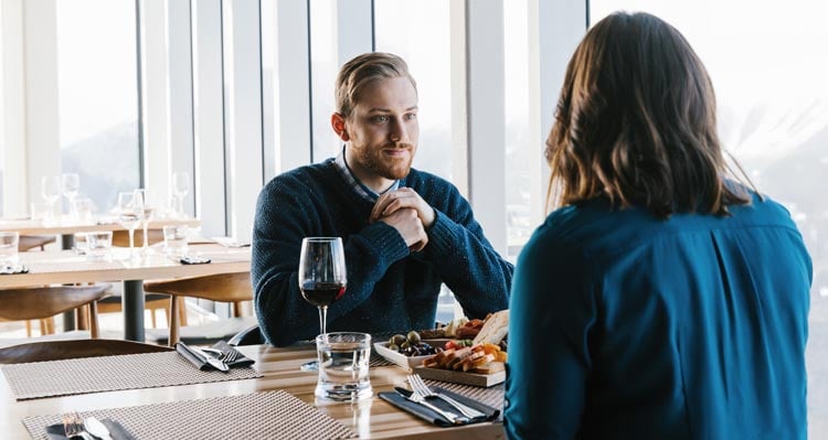 A couple sit for dinner at a window-side table with natural sunlight coming through.