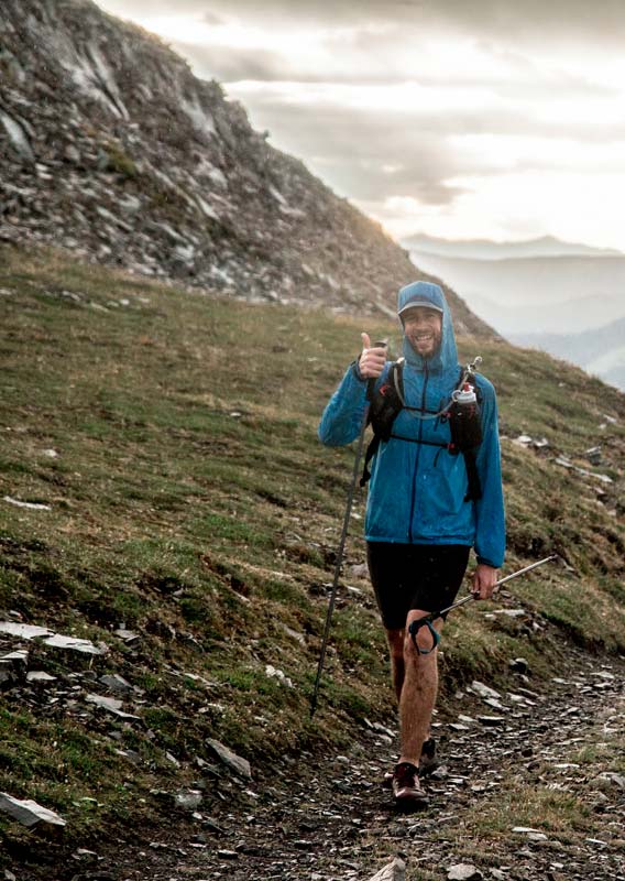 A man in a blue sweater walks along a path in a mountain meadow