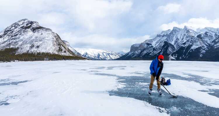 A person skating on a frozen lake surrounded by mountains.