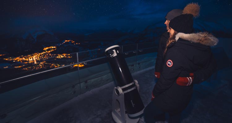 Two people stargaze high above a lit town.