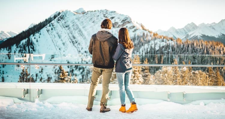 Two people stand at a viewpoint looking towards a mountain vista.