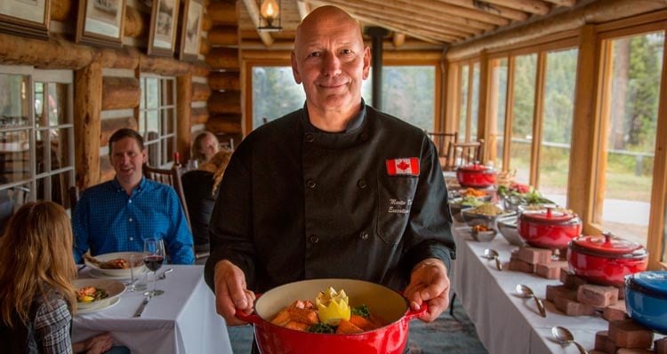 Chef Martin Brenner holds a ceramic pot of food in a historic chalet