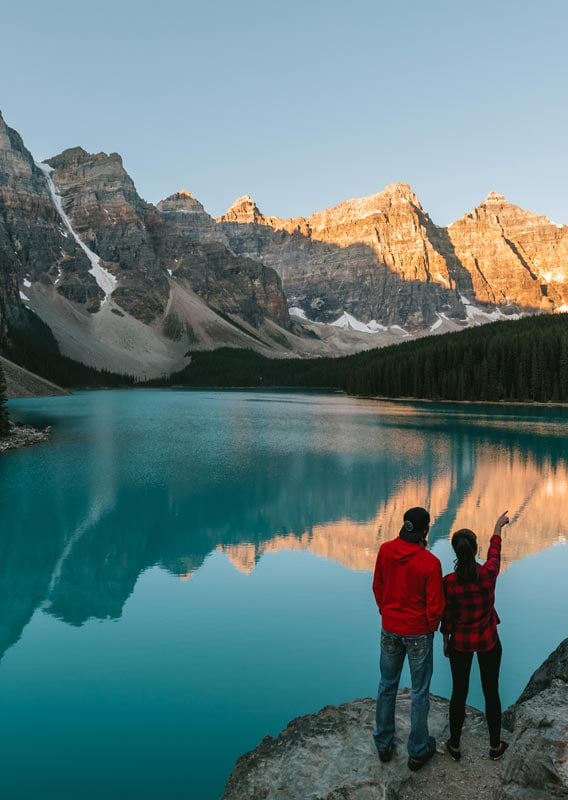 Two people stand above Moraine Lake, looking at mountains.
