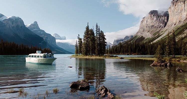 A boat approaches a small tree-covered peninsula and lake-shore.