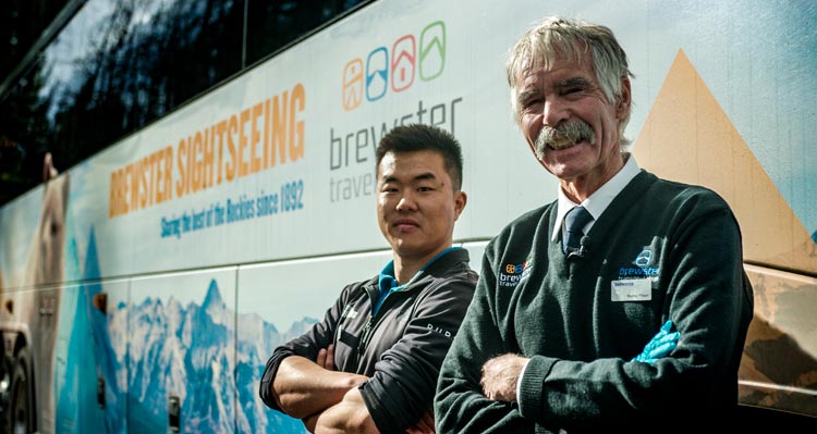 Two bus drivers stand outside a sightseeing bus.