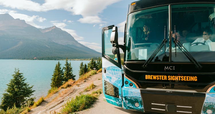 A bus stopped at the side of the road above a blue lake.