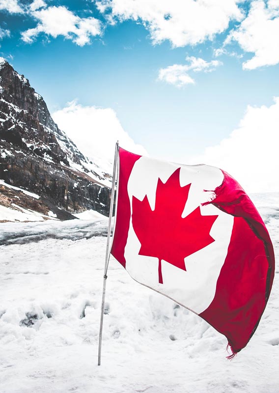 A Canadian flag on a glacier below mountains.