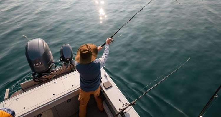 A fisher casts a rod from a small boat into a still lake.