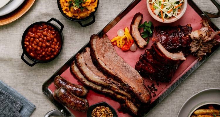 A platter of smokehouse brisket, sausages, ribs and barbecue side dishes.