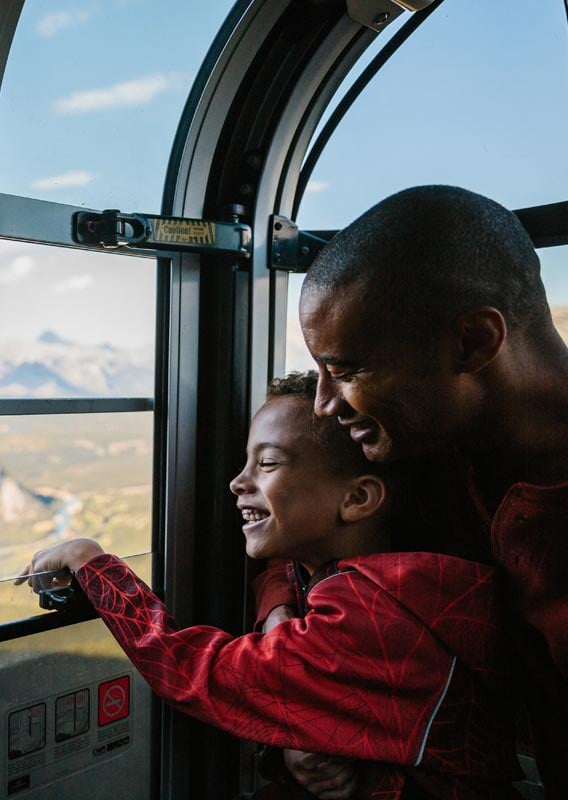 A dad and child look out the window of a Banff Gondola cabin.