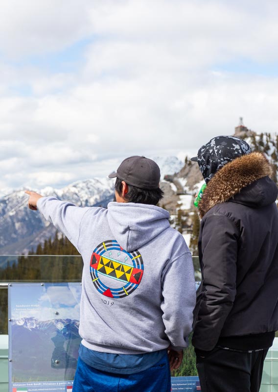 Two teenagers look out from the Banff Gondola viewing deck across a wide valley