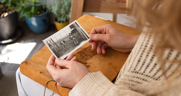 A woman holds a black and white photo over a leather-bound album