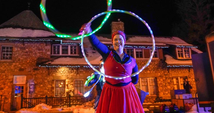 A dancer with two hoops dances on a nighttime outdoor day.