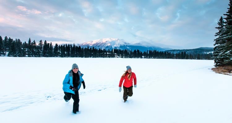 Two people run across a snowy field.