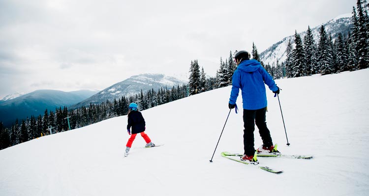 A parent and child ski down the snowy hill at Marmot Basin.