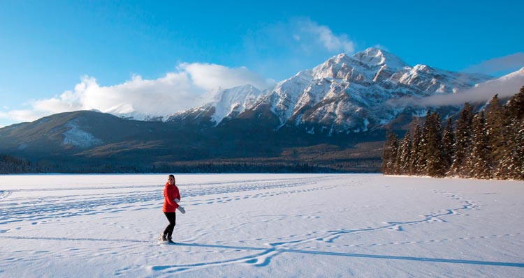 A person in a red jacket stands on a snowy field in front of a snow-covered mountain.