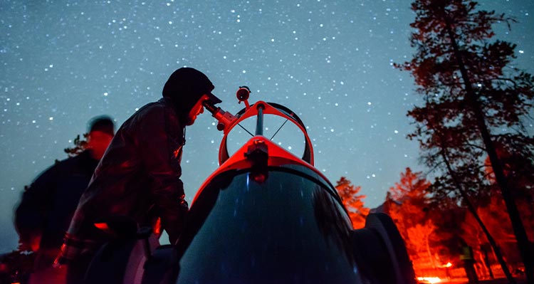 A person looks into a telescope under a starry night sky.