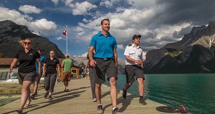 A group of people walk down a dock beside a large lake.