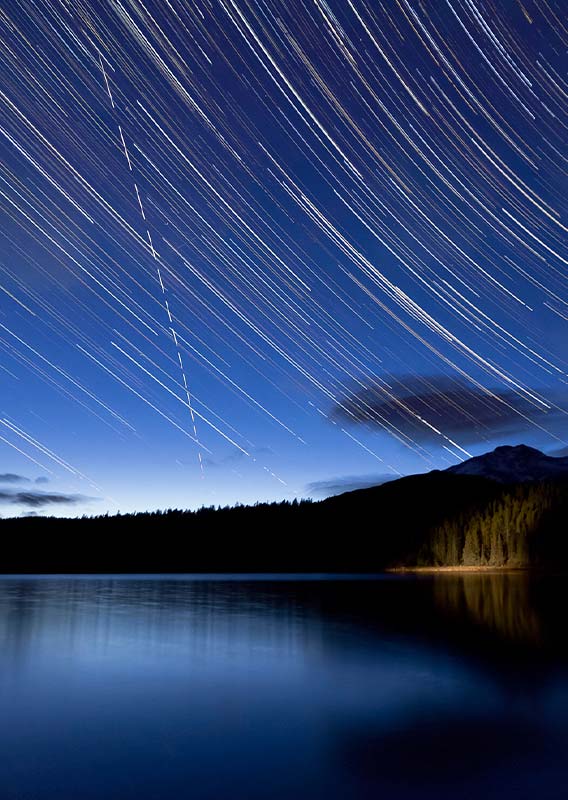 A timelapse view of stars moving across the night sky above a lake