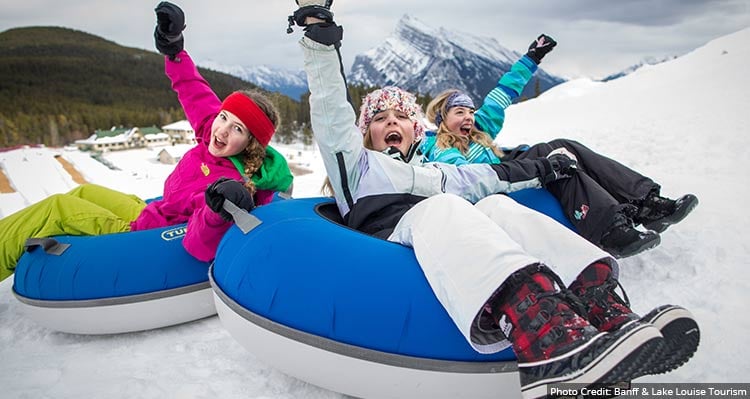 Three kids in snow tubes going down a snowy hill