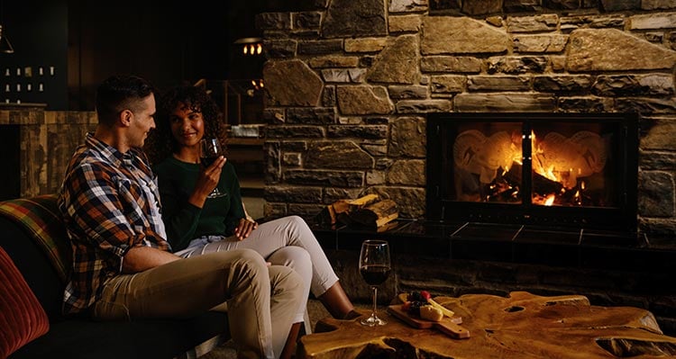Two people sit in a lounge next to a fireplace.