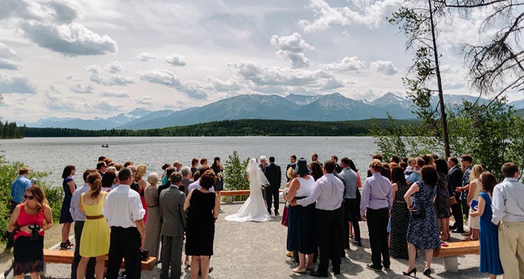 A wedding ceremony in front of a large lake below tree-covered mountains.