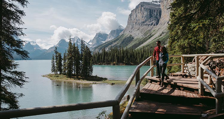 Two people walk on a boardwalk near a small peninsula.