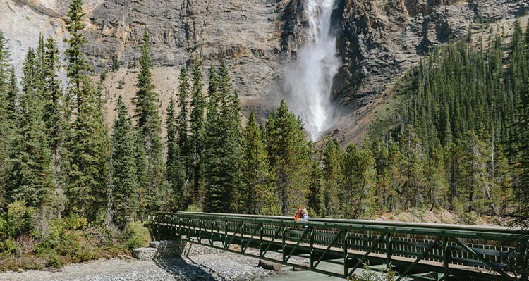 A bridge over a river towards a a splashing waterfall.