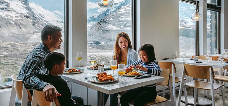 A family sits in a restaurant window with mountains in the view