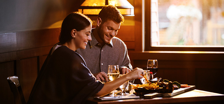 A couple sits at a booth sharing food and wine