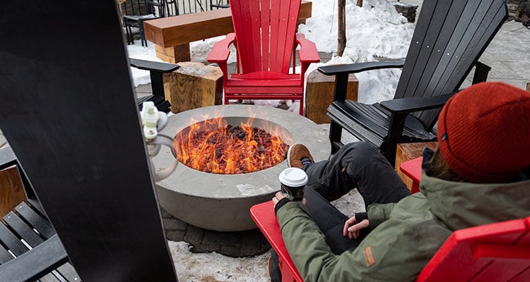 A guest sits by a fire pit with a hot beverage in hand