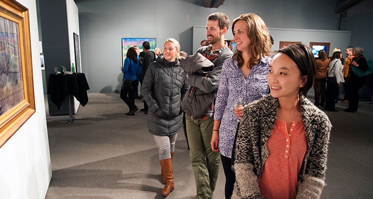 A group of people observe a piece of artwork hanging on the wall of a gallery