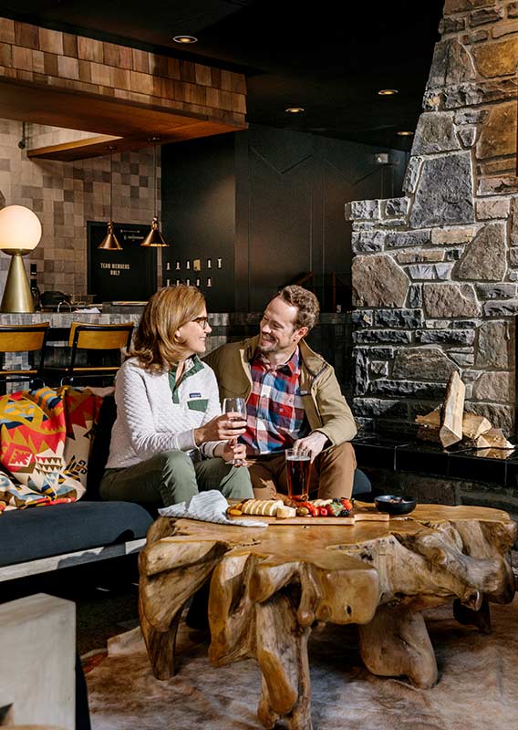 A couple sits by a fire with beverages and tapas