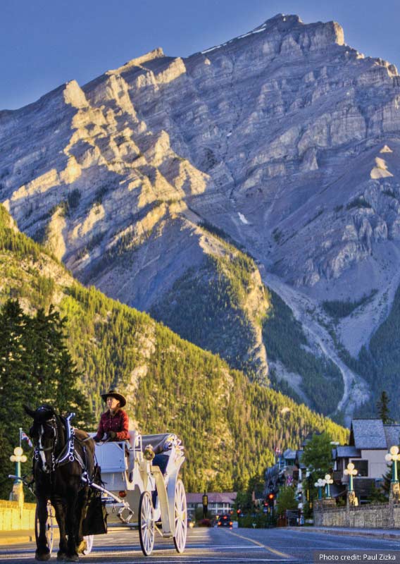 A horse and buggy stroll down a Banff street with a mountain in the background