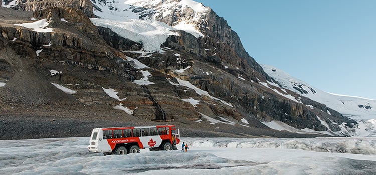 An icefield explorer roams through snow below a mountain