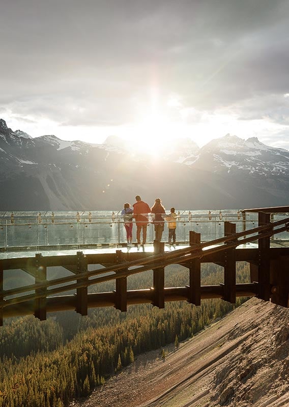 A family stands at the edge of the Columbia Icefield Skywalk glass rail admiring the sunset