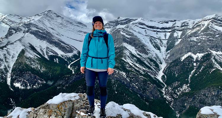 A hiker stands on rocks before a vista of snow-covered mountains.