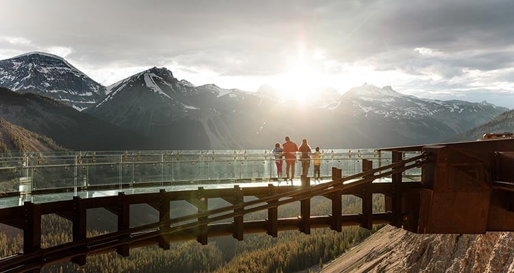 A family stands on a glass platform above a wide valley.