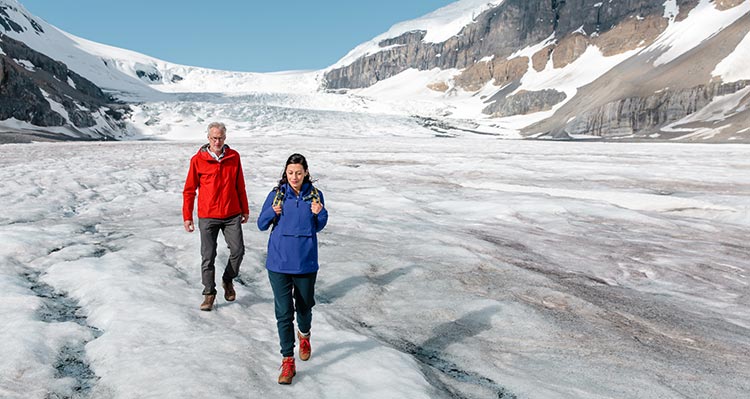 Two people walk on a glacier below the large Columbia Icefield.