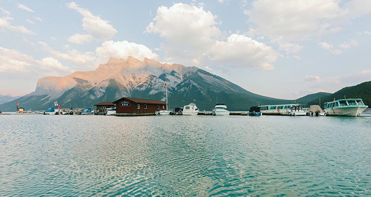 A dock with boats on a lake below a tree-covered mountain.