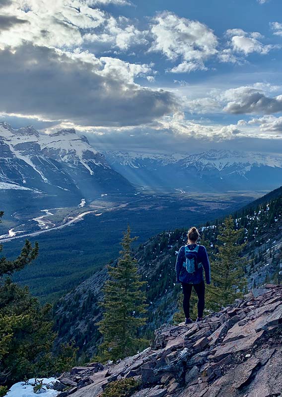 A hiker stands on a rock high above a wide forested valley.