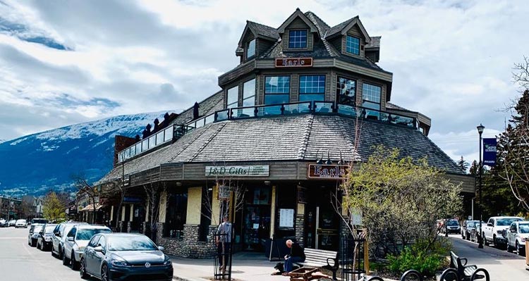 A street corner building with a rooftop patio and mountains behind in the distance.