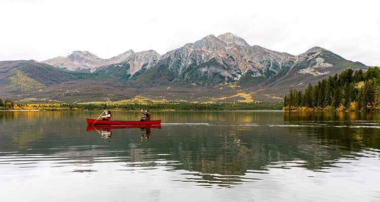 A canoe glides along a clear lake below tall mountains.