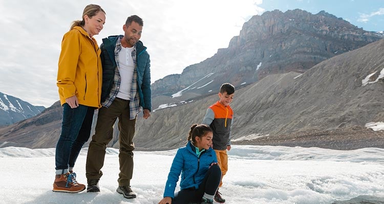 A family stands on the Athabasca Glacier below tall mountains.